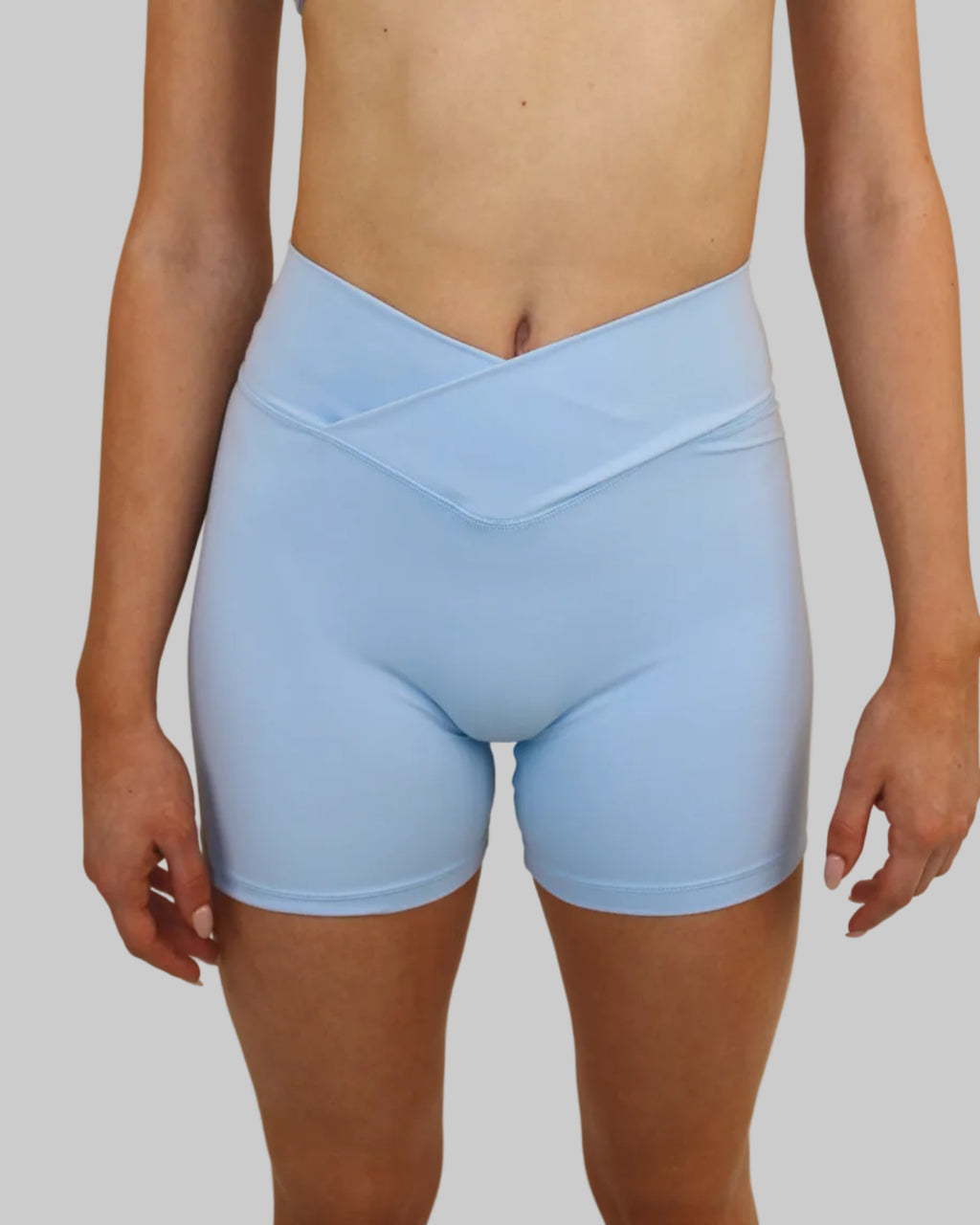 A model wearing a light blue two-piece activewear set consisting of a sports bra and high-waisted biker shorts, shown from the chest down against a plain beige background.