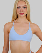 A blonde woman modeling a light blue scoop-neck bralette against a plain beige background.