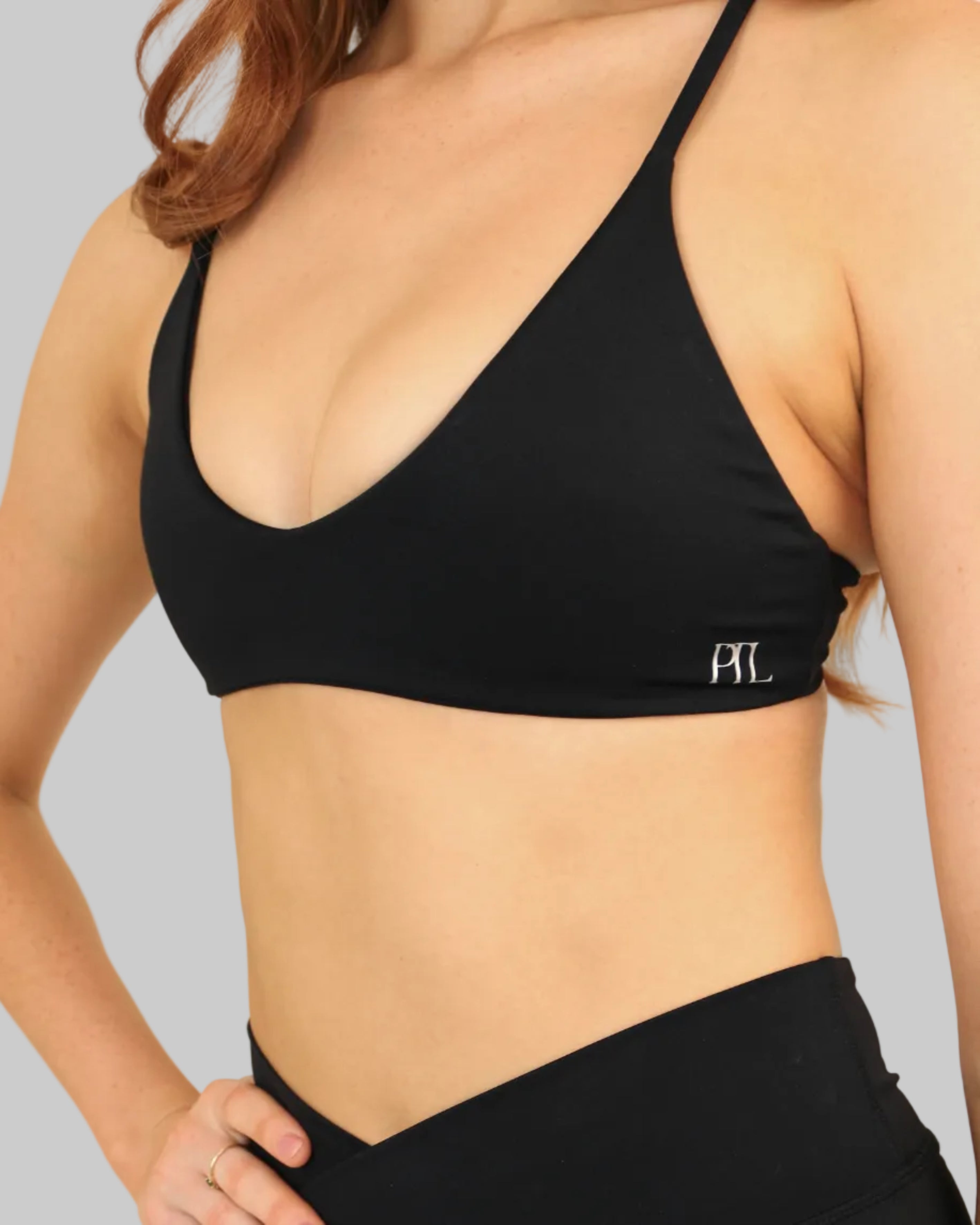 A woman wearing a black sports bra and matching high-waisted black athletic shorts against a plain beige background.