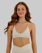A woman modeling a matching off-white activewear set consisting of a sports bra and high-waisted shorts, set against a plain light beige studio background.