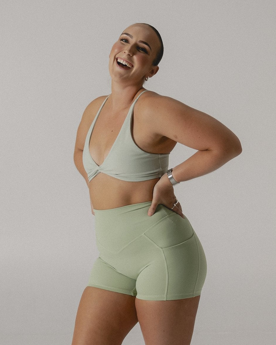 Person wearing a green sports bra and shorts set on a plain background
